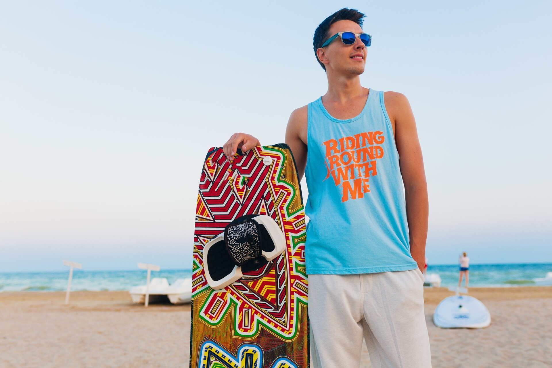 young-athletic-man-with-kite-surfing-board-posing-beach-wearing-sunglasses-summer-vacation_285396-10230